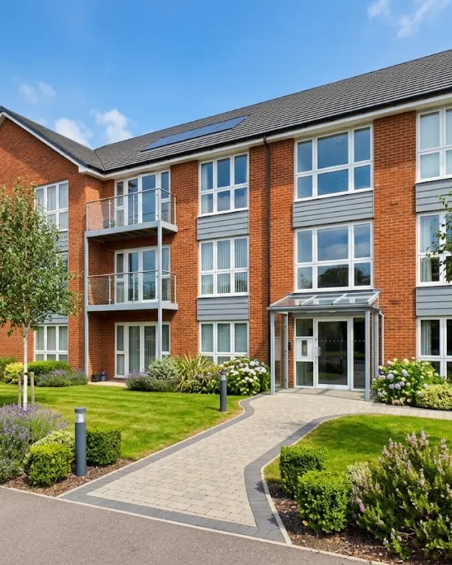 Three-storey red-brick apartment building with balconies and a landscaped garden
