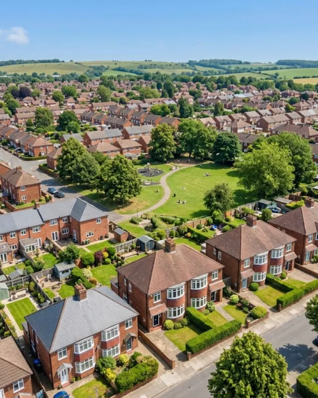 View across streets of red-brick houses, gardens and a park, with hills beyond