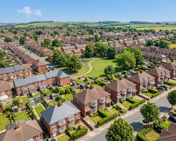 View across streets of red-brick houses, gardens and a park, with hills beyond