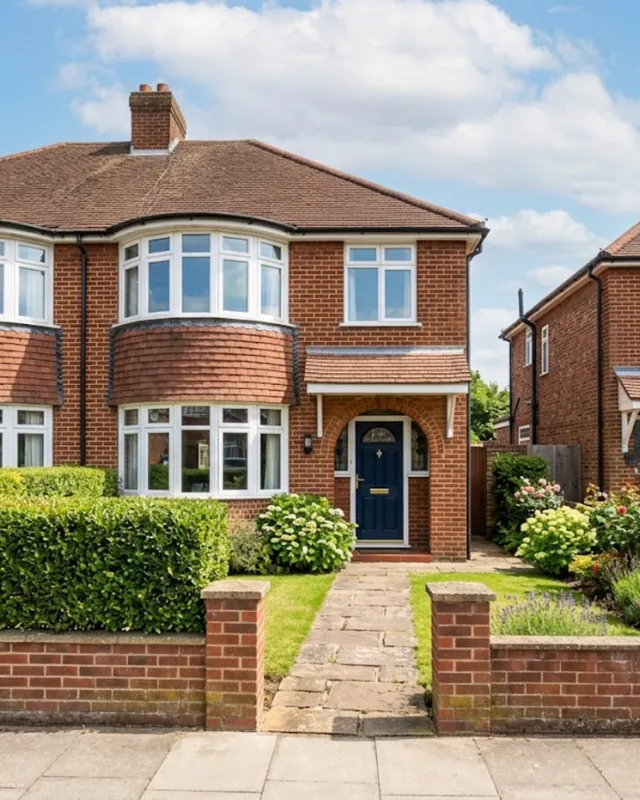 Red-brick semi-detached house with bay windows, a navy front door and a hedged front garden